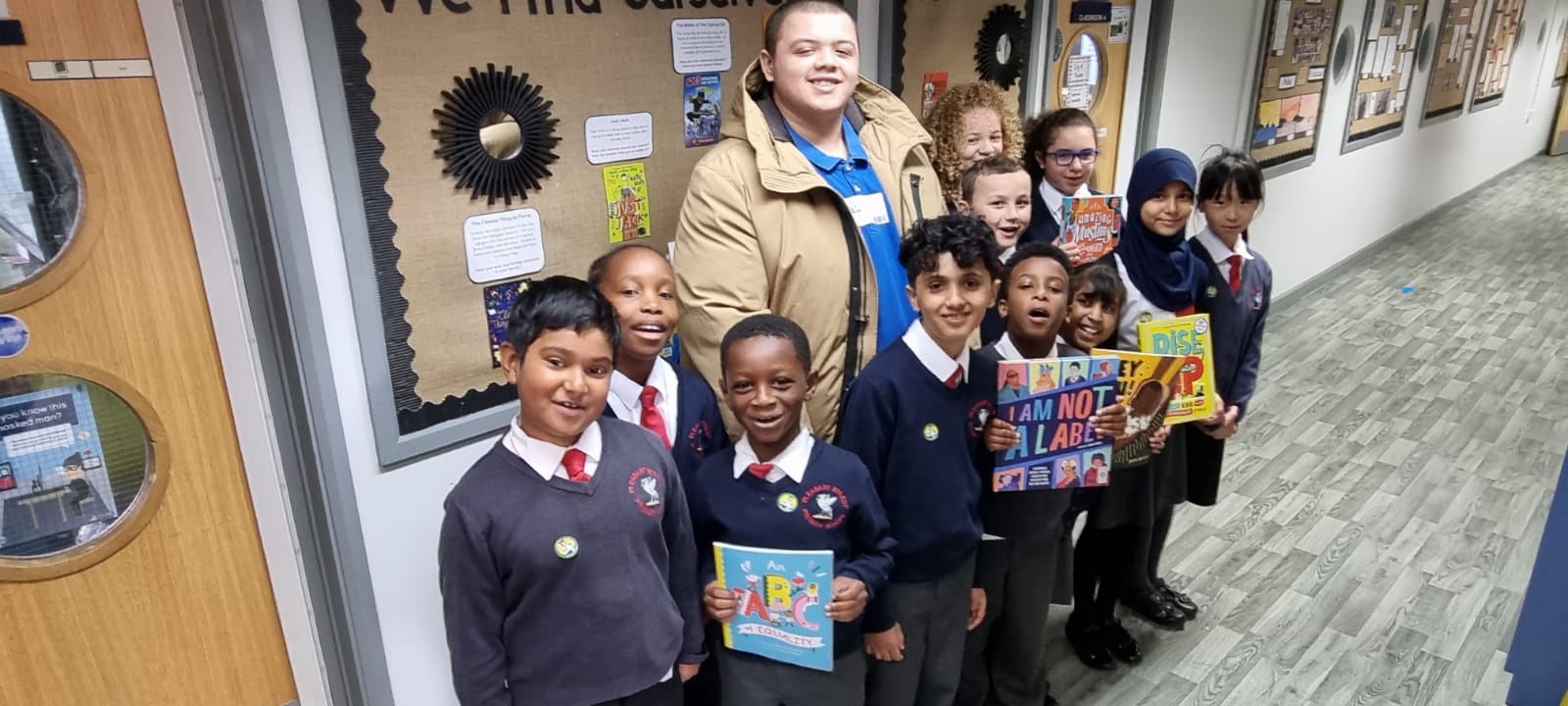 Wade Holligan poses with students from Pleasant Street Primary School. They hold up books from the collection in front of them.